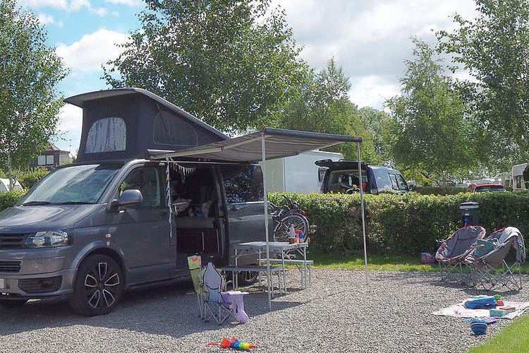 A VW T5 camper with a pop top roof and an awning, set up ready for camping in the sunshine