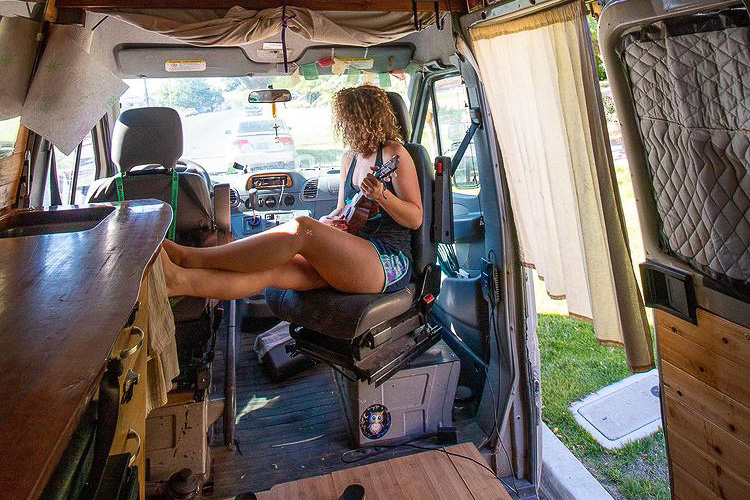 A lady sits in her passenger swivel seat playing the ukulele in her campervan