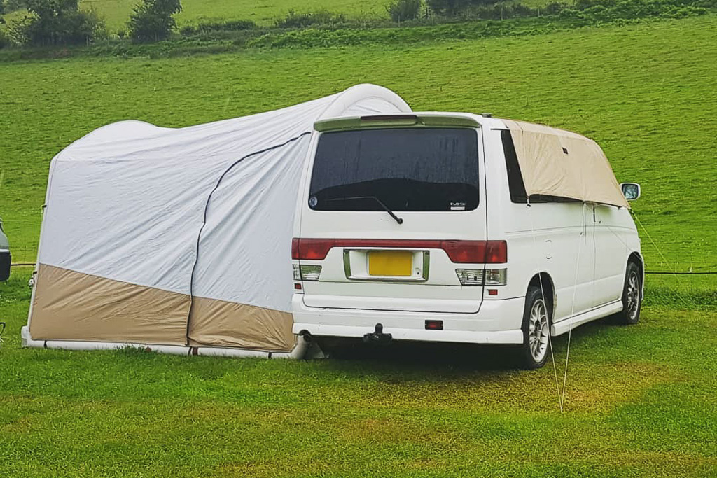 A short wheelbase campervan sits in a field with a drive away awning attached to the side.