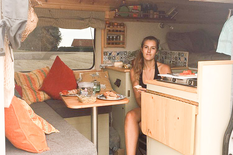 A lady sitting ready for lunch at a removable island table in her DIY campervan conversion