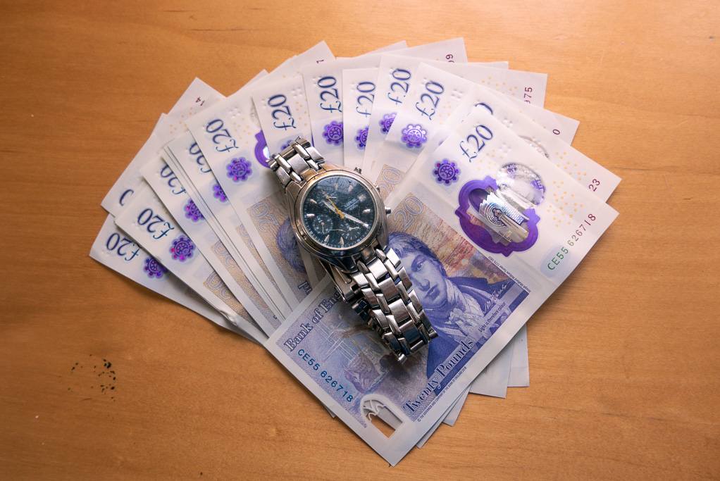 A watch on top of a spread of twenty pound notes