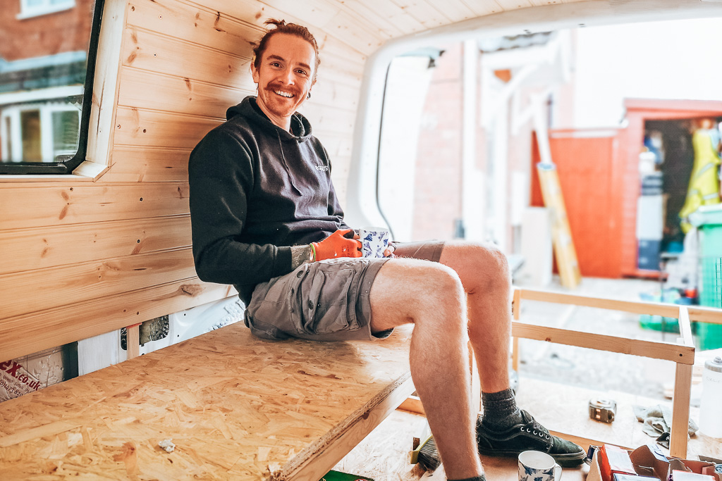 A man sitting on completed seating in a DIY campervan