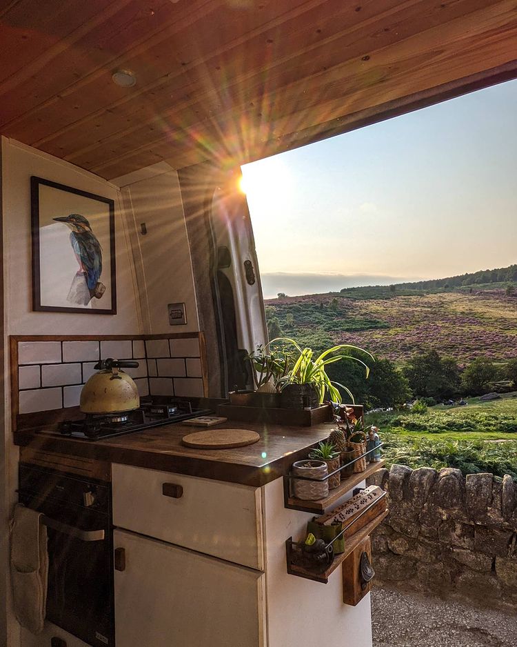 A kitchen in a campervan layout, next to an open door with a view of the English countryside