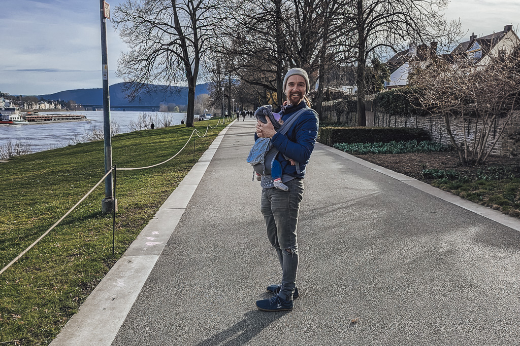 A man with a baby carrier on a path along side the Rhine River leading to Koblenz