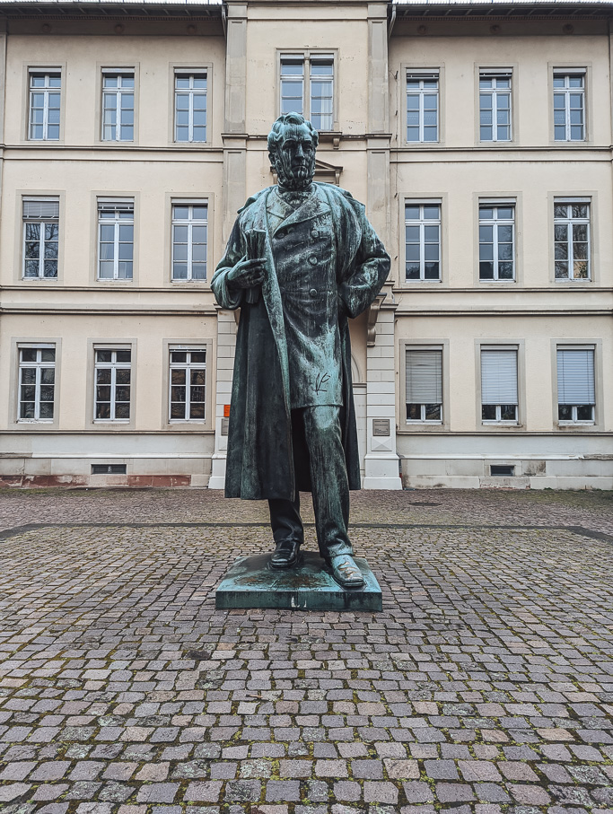A bronze statue of Robert Bunsen in front of a white traditional building